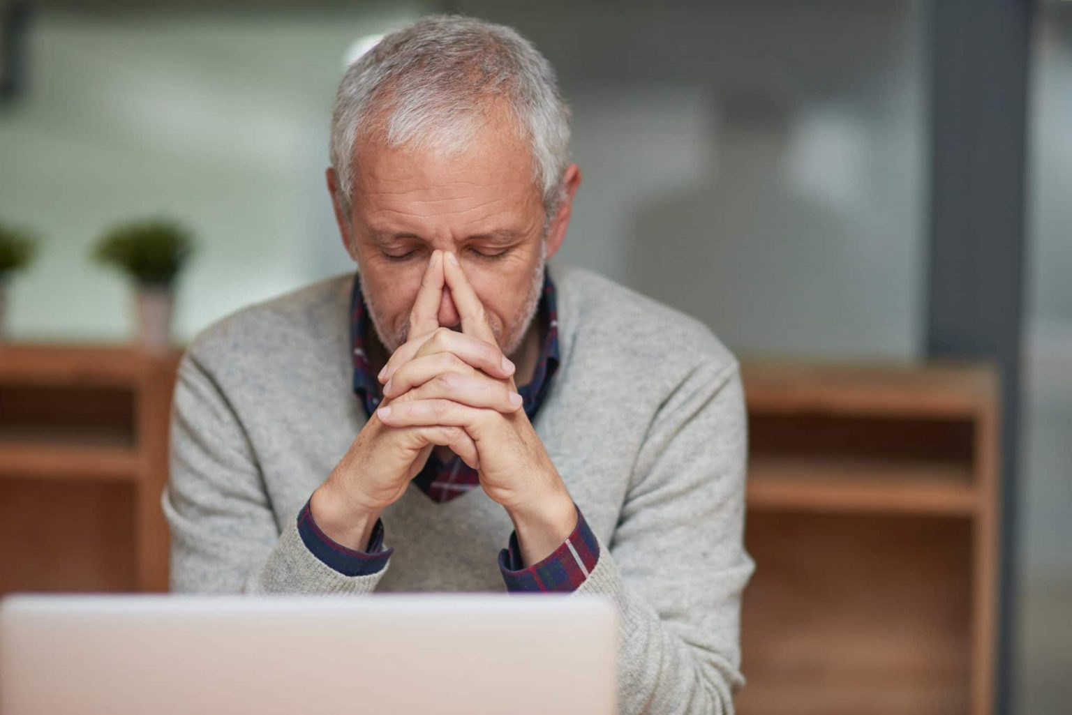 Older man has his hands clasped together with index fingers on bridge of nose
