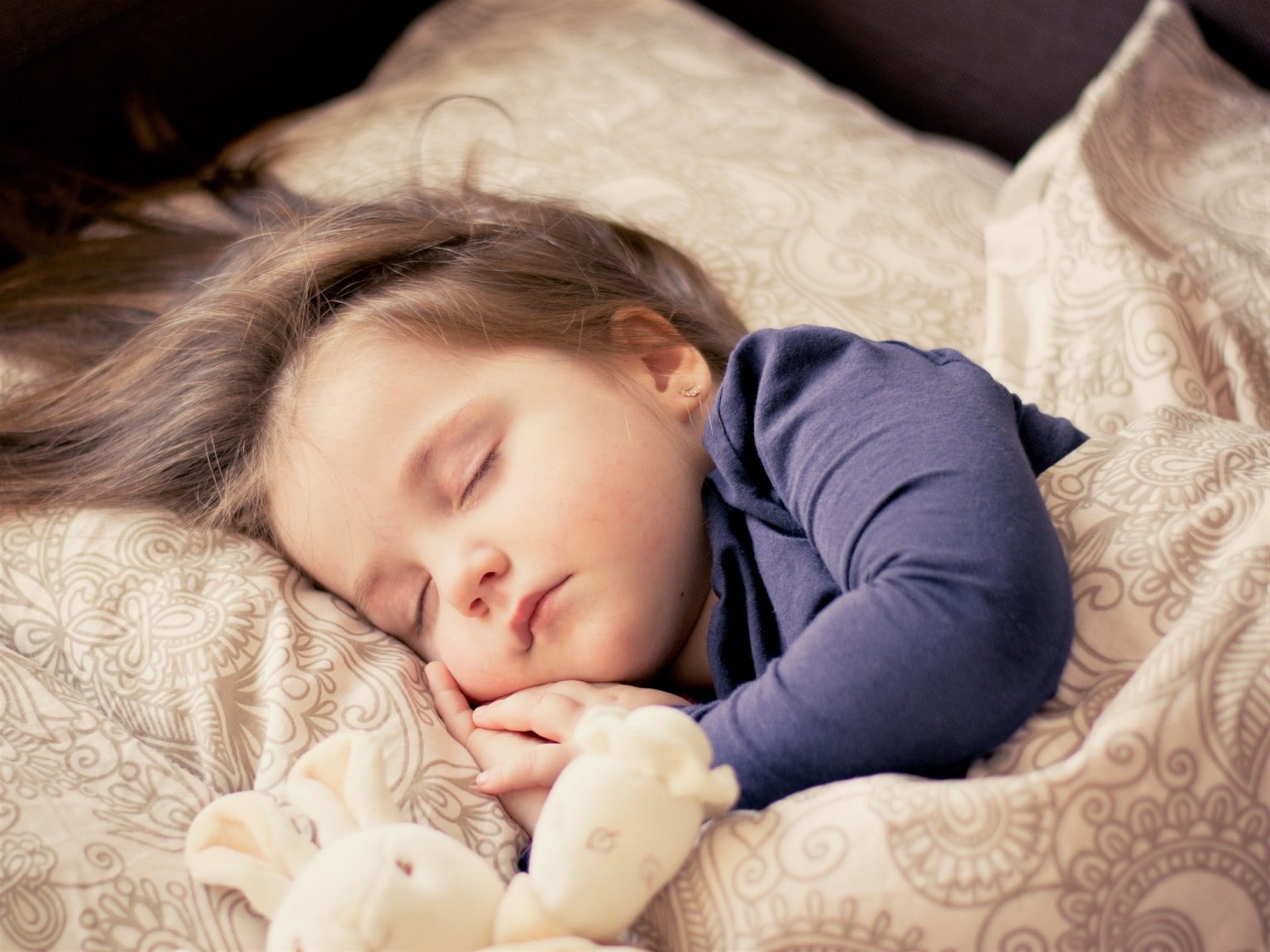A female toddler sleeping in bed with a stuffed animal.